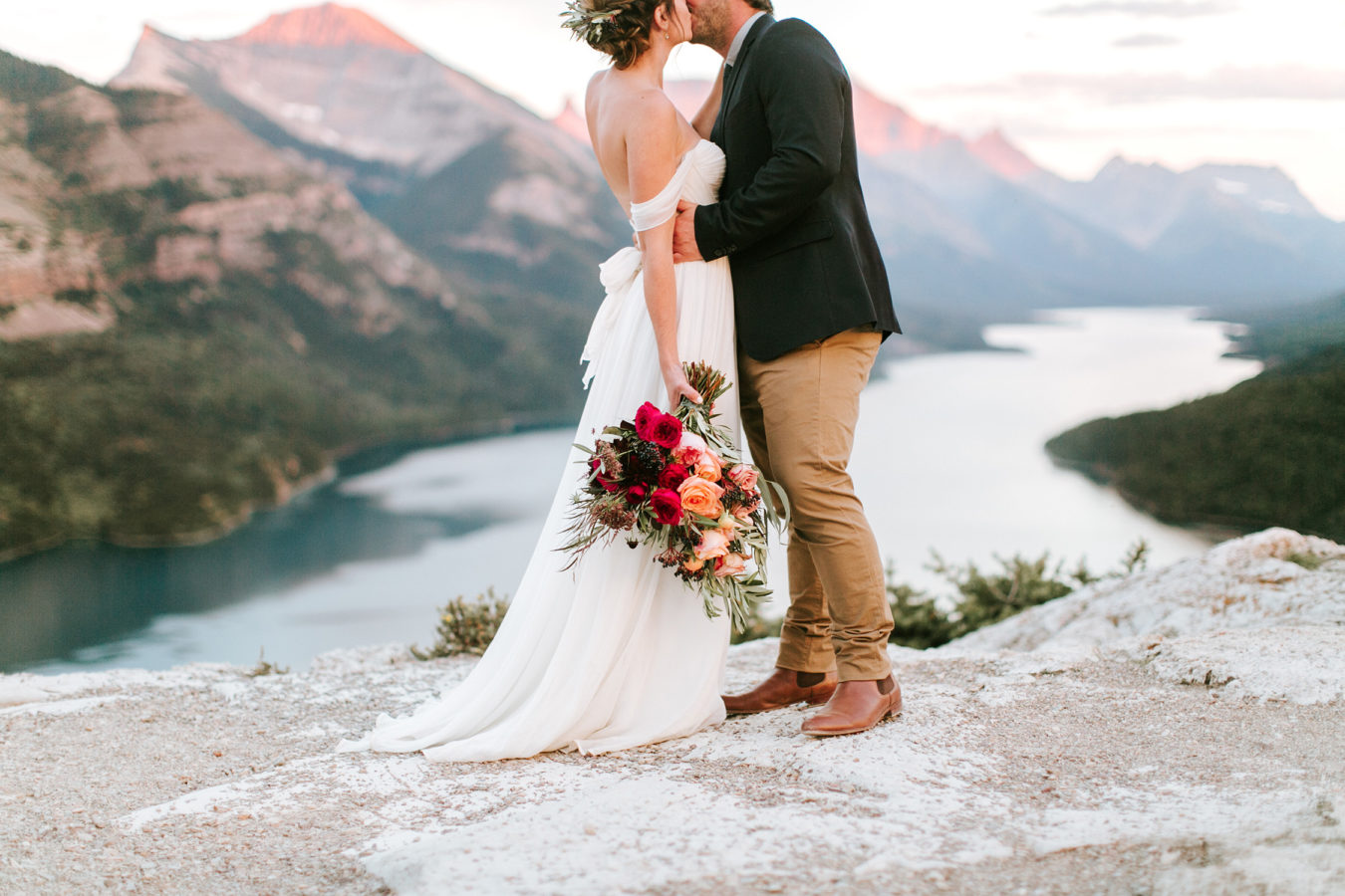 bride and groom kissing while view of lake and mountains are behind them
