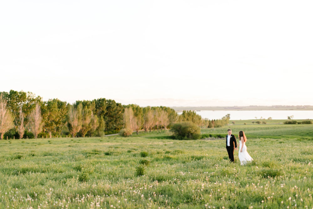 bride and groom walk threw a grassy meadow at rocking R guest ranch at sunset