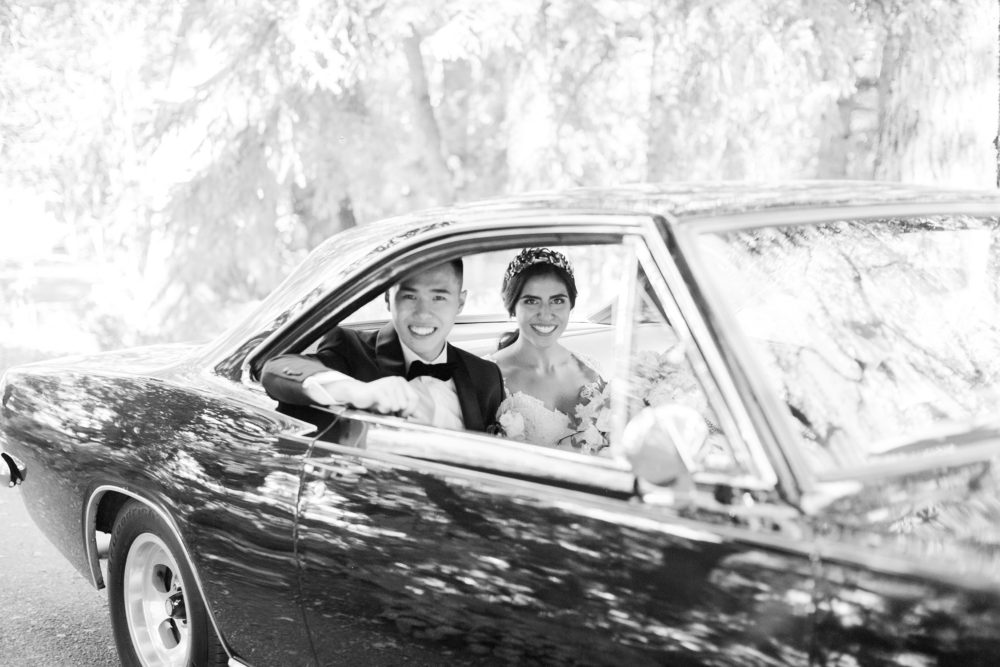 bride and groom exit wedding in a black vintage car